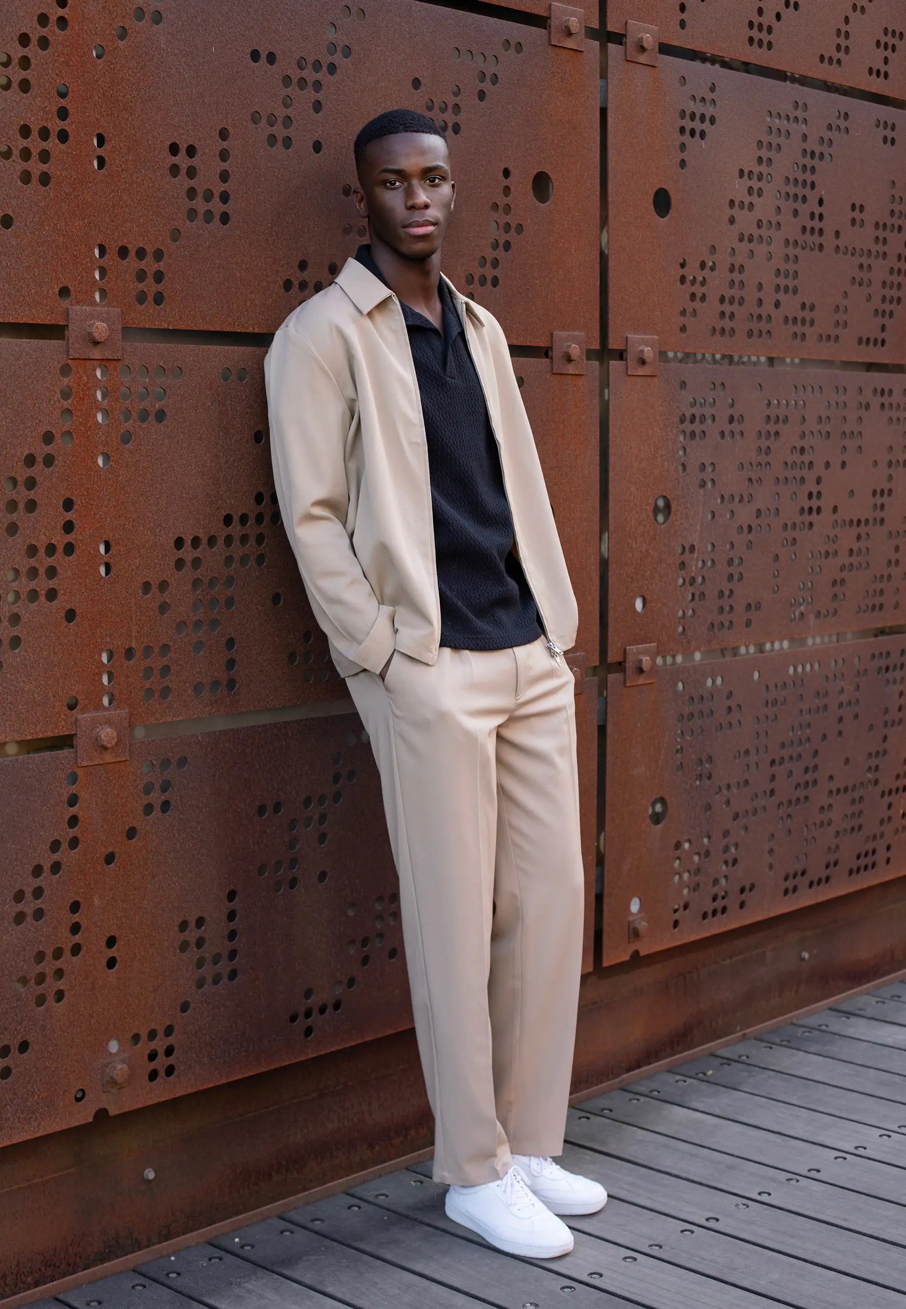 Man in beige coat and black shirt against a textured wall