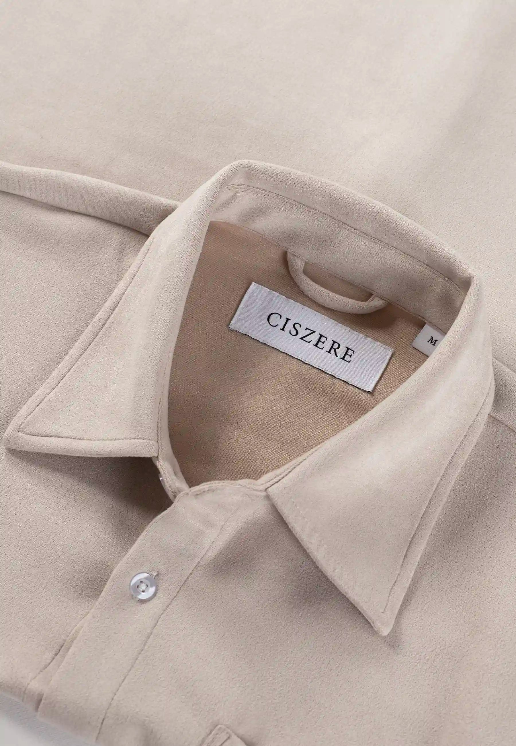 Närbild på kragen till en beige skjorta från märket CISZERE. Vit etikett med svart text "CISZERE" och storleksetikett "M" syns på insidan av kragen. En vit knapp är knäppt på framstycket.