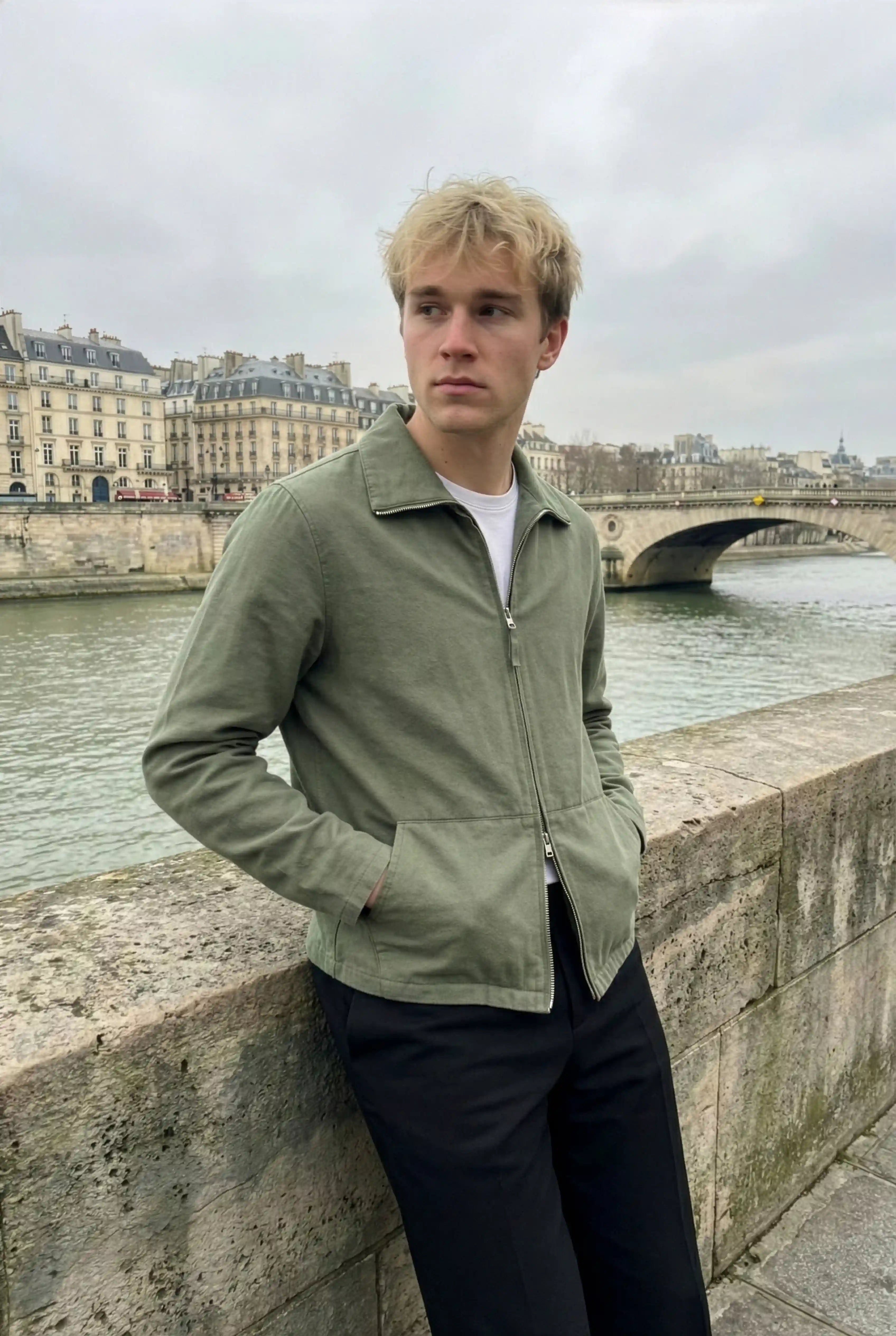 Man in a green canvas jacket and dark trousers by a river in Paris