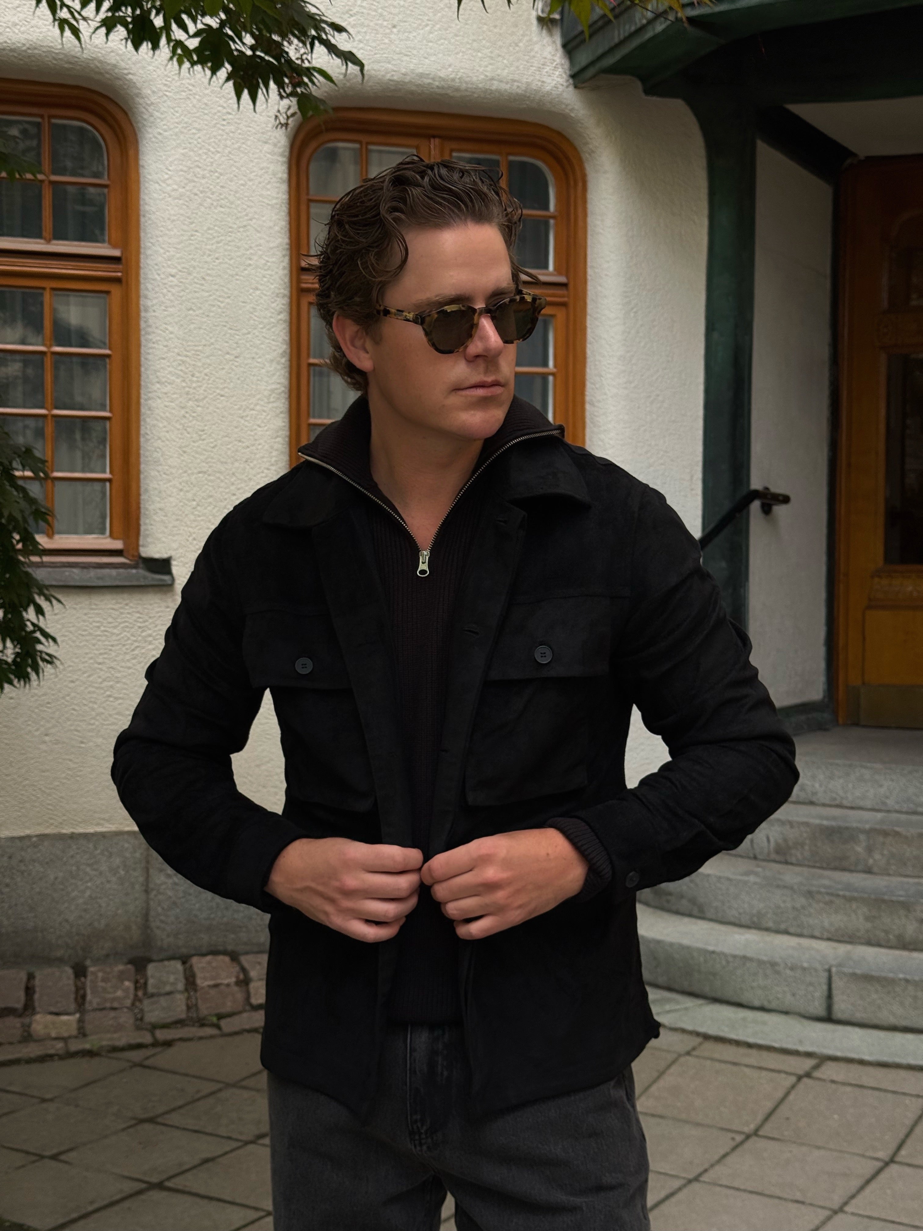 Martin Hansson in a black suede overshirt and half-zip knit outside a Nordic villa