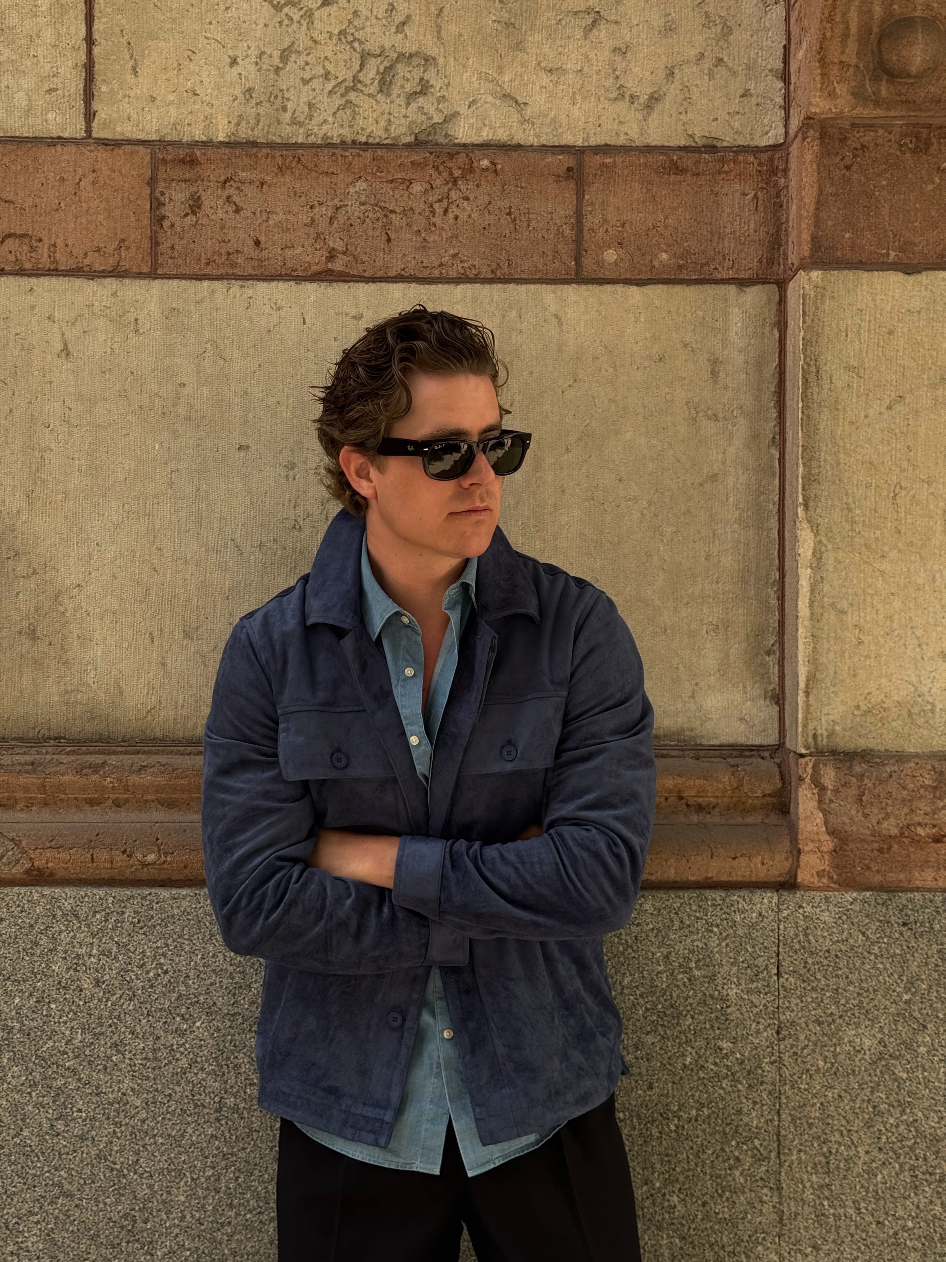 Martin Hansson in a blue suede overshirt leaning against a stone wall