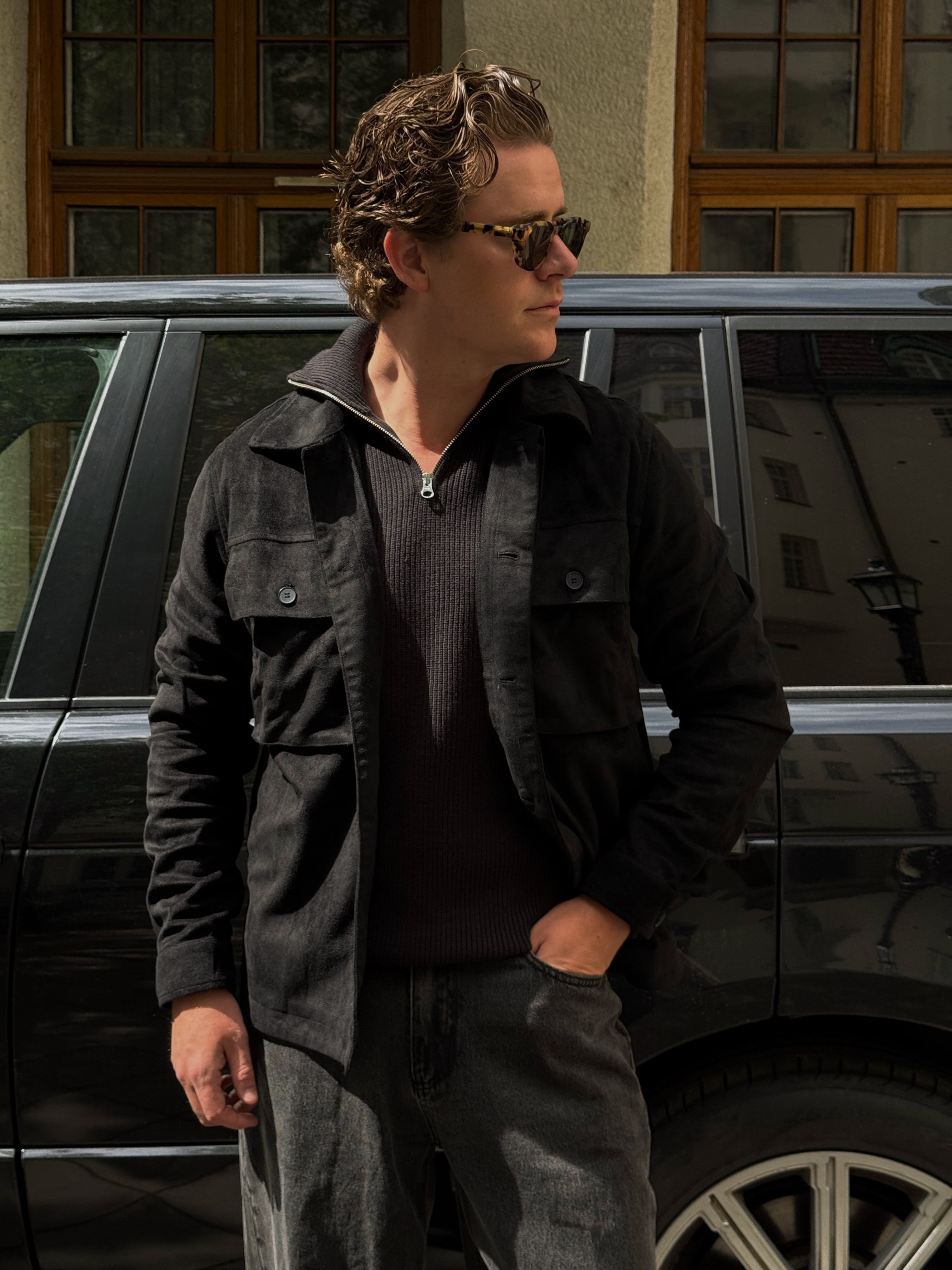 Martin Hansson in a charcoal overshirt and brown half-zip beside a dark car